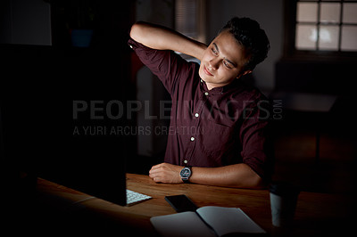 Buy stock photo Shot of a young businessman experiencing neck pain while working on a computer in an office at night