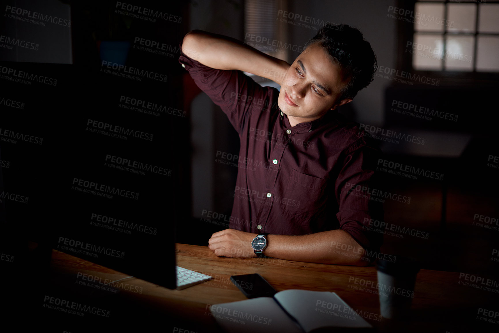 Buy stock photo Shot of a young businessman experiencing neck pain while working on a computer in an office at night
