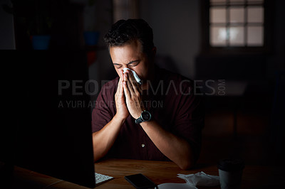 Buy stock photo Shot of a young businessman blowing his nose while working in an office at night