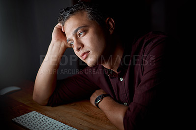 Buy stock photo Shot of a young businessman looking bored while working on a computer in an office at night