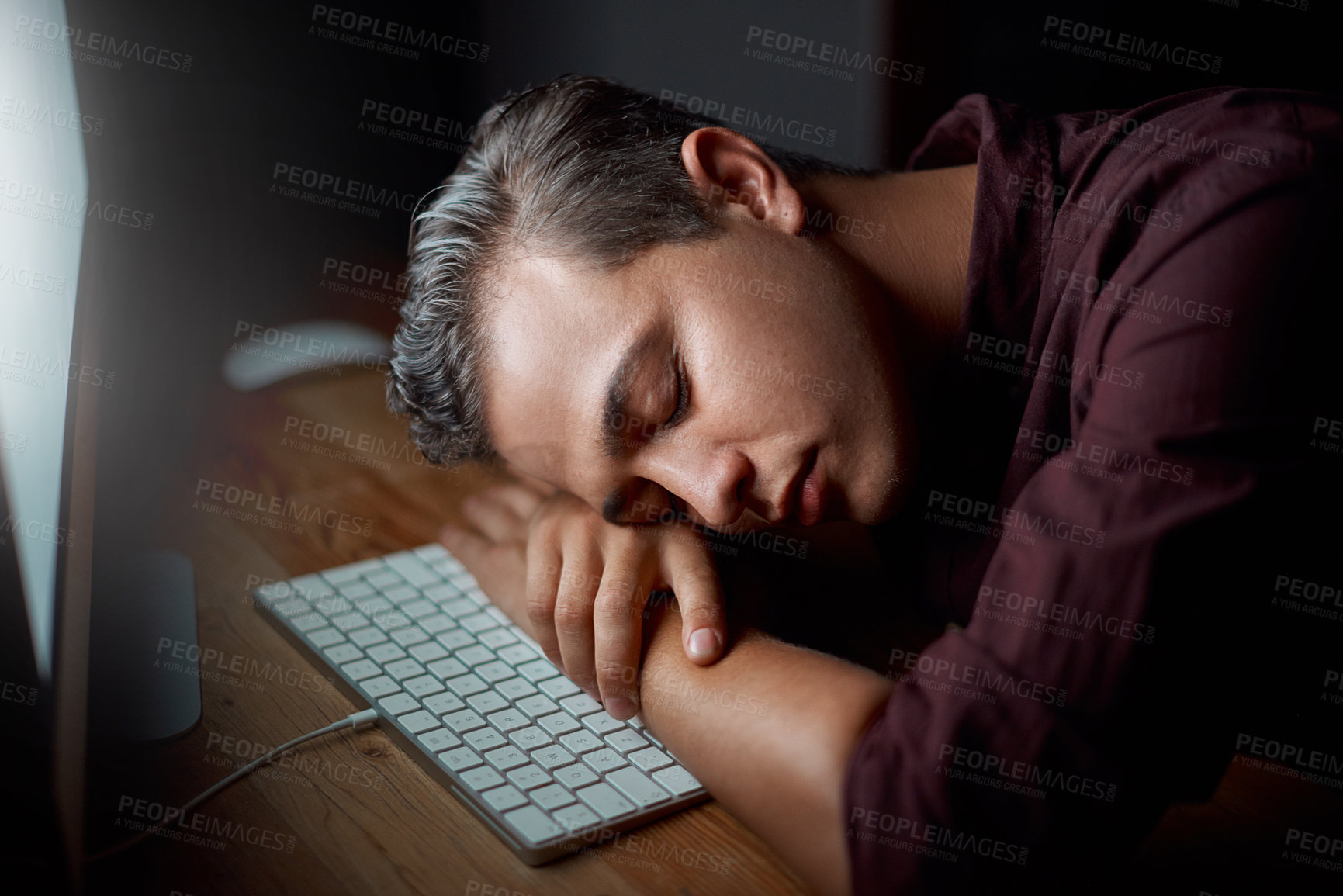 Buy stock photo Shot of a young businessman sleeping at his desk while working in an office at night
