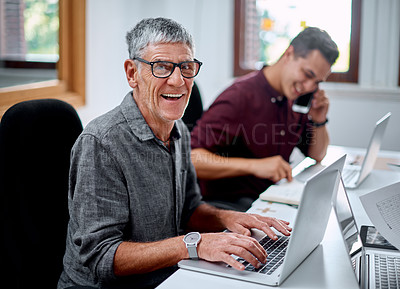 Buy stock photo Portrait of a senior businessman working on a laptop in an office with a colleague in the background