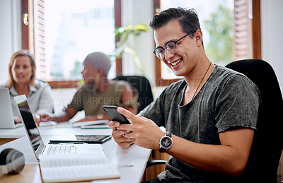 Buy stock photo Shot of a young businessman using a cellphone while working in an office