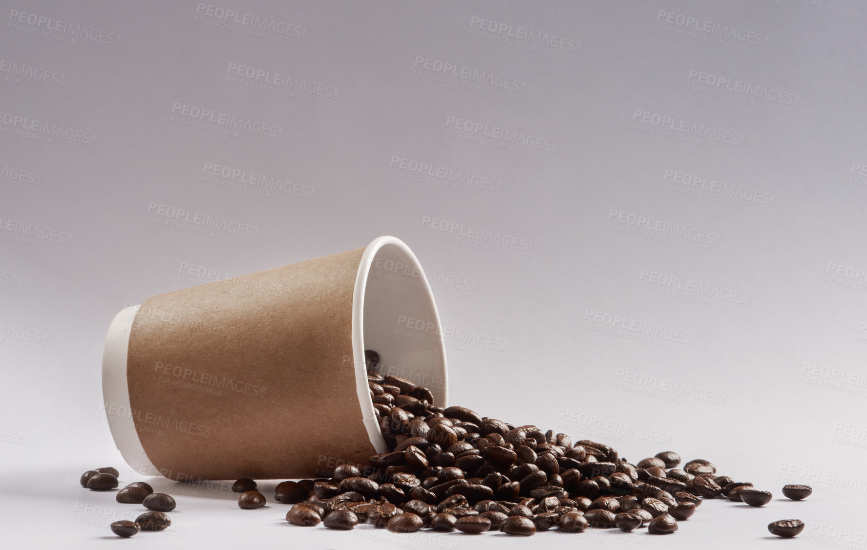 Buy stock photo Studio shot of a tipped over paper cup filled with coffee beans against a grey background