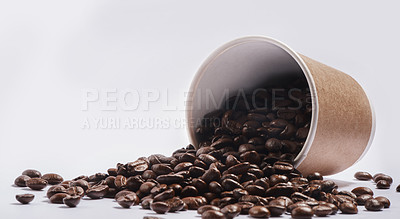 Buy stock photo Studio shot of a tipped over paper cup filled with coffee beans against a grey background