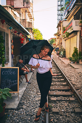 Buy stock photo Shot of a young woman holding an umbrella while exploring a foreign city on a sunny day