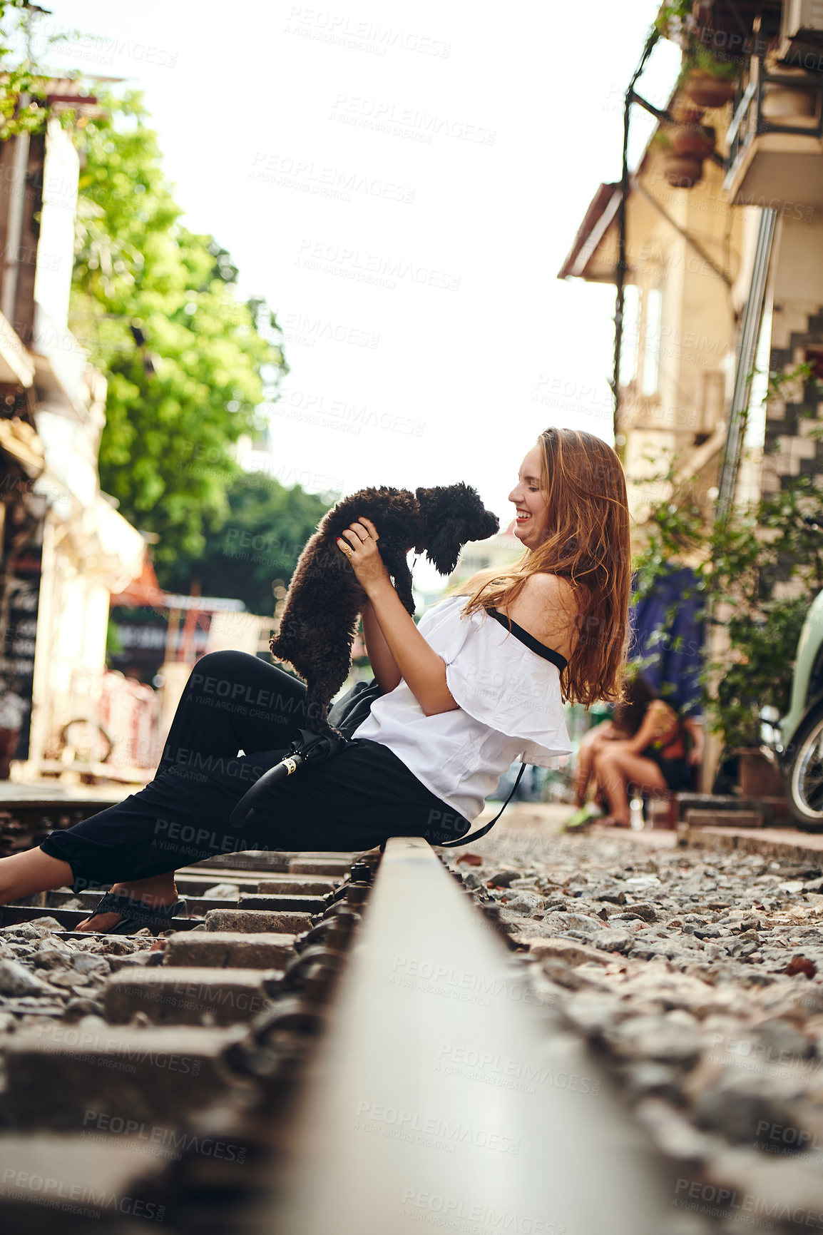 Buy stock photo Shot of a young woman playing with a dog while exploring a foreign city