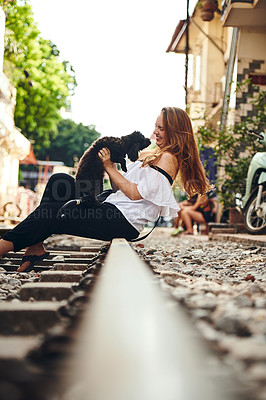 Buy stock photo Shot of a young woman playing with a dog while exploring a foreign city