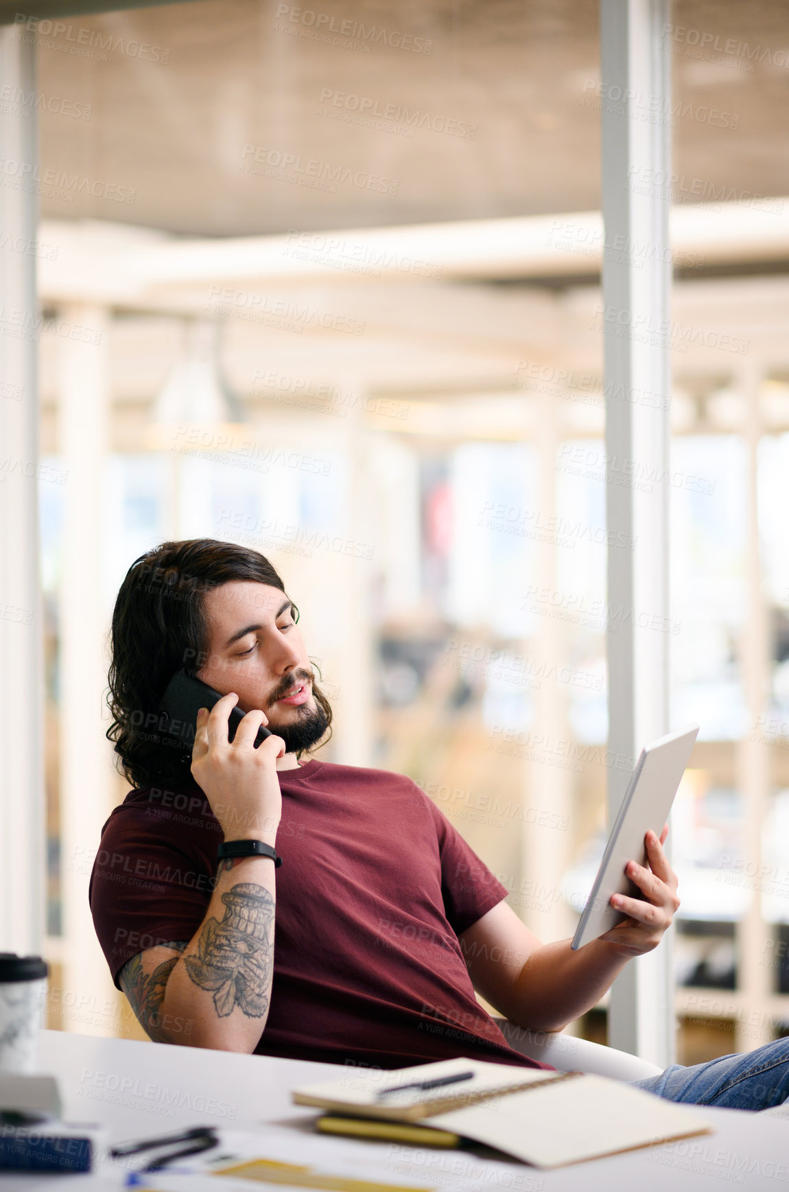 Buy stock photo Shot of a young businessman talking on a cellphone while using a digital tablet in an office