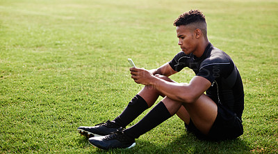Buy stock photo Shot of a young man sitting on the field and using a smartphone at a rugby match