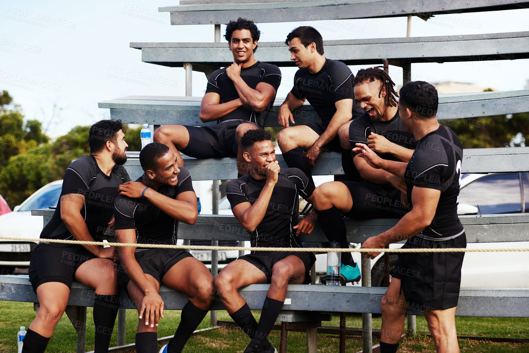 Buy stock photo Shot of a group of young men sitting on the benches together at a rugby game
