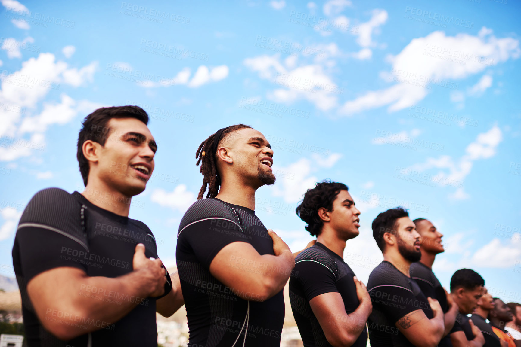 Buy stock photo Shot of a team of young rugby players singing the national anthem before a game
