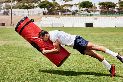 Buy stock photo Shot of a young rugby player training with a tackle bag on the playing field