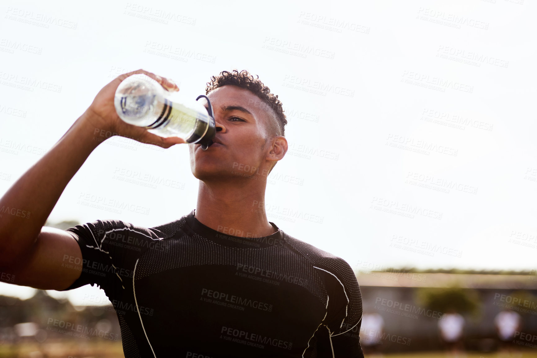 Buy stock photo Shot of a young man drinking water after playing a game of rugby