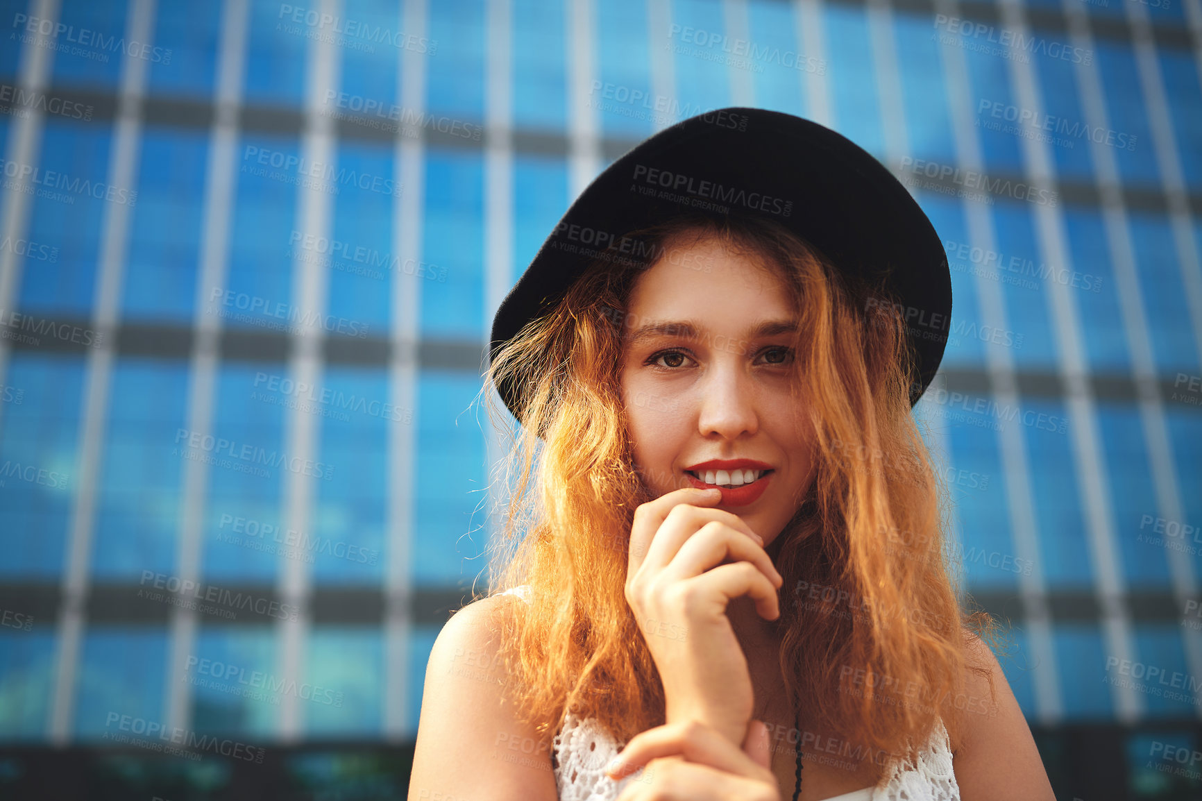 Buy stock photo Shot of a beautiful young woman posing outside against a glass building