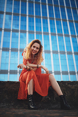 Buy stock photo Shot of a beautiful young woman sitting outside against a glass building