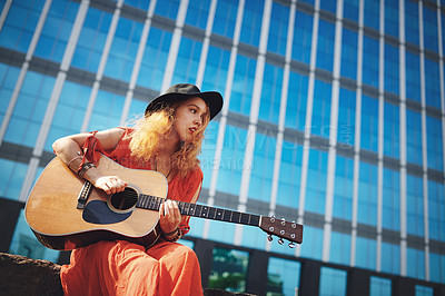 Buy stock photo Shot of a beautiful young woman playing the guitar while out in the city