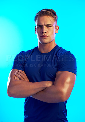 Buy stock photo Studio portrait of a handsome young male athlete standing with his arms folded against a blue background