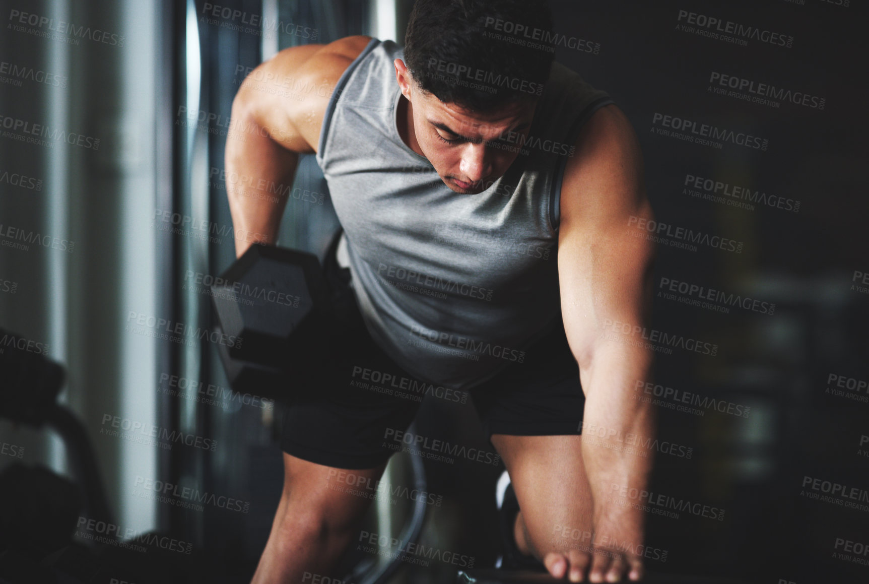 Buy stock photo Shot of a sporty young man exercising with a dumbbell at the gym