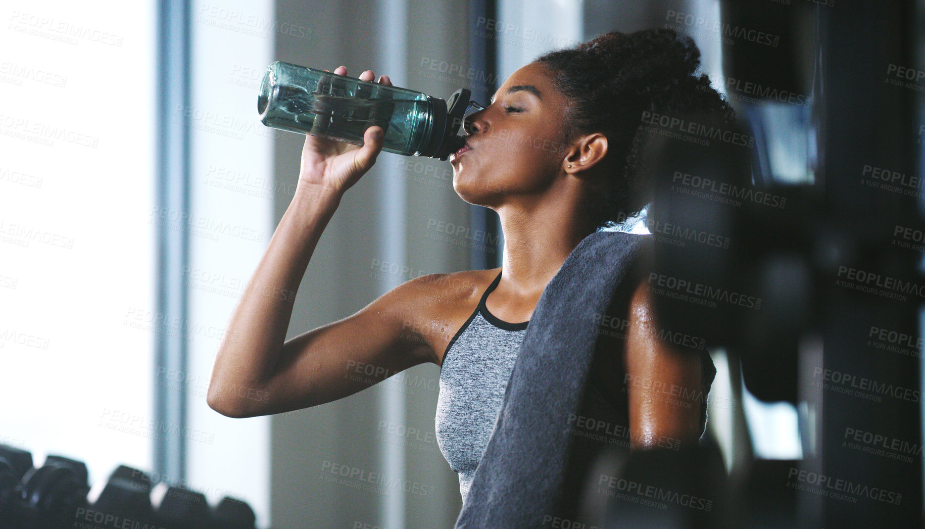 Buy stock photo Shot of a sporty young woman drinking water while exercising at the gym