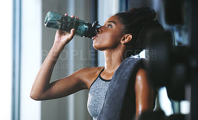 Buy stock photo Shot of a sporty young woman drinking water while exercising at the gym