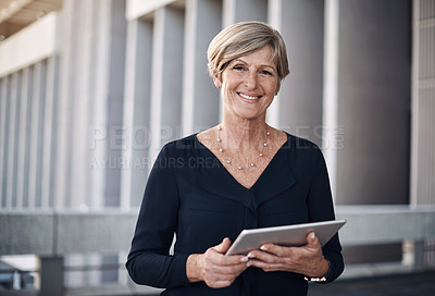 Buy stock photo Shot of a mature businesswoman using a digital tablet against a city background
