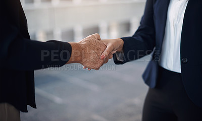Buy stock photo Cropped of two businesswomen shaking hands against a city background