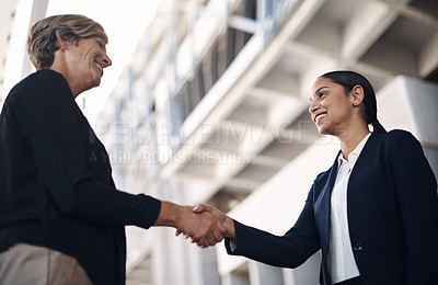 Buy stock photo Shot of two businesswomen shaking hands against a city background