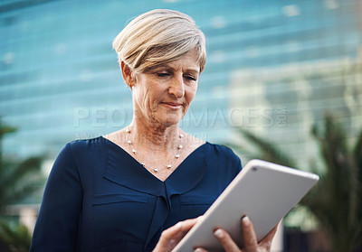 Buy stock photo Shot of a mature businesswoman using a digital tablet against a city background