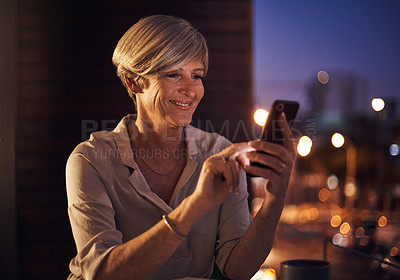 Buy stock photo Cropped shot of an attractive mature businesswoman sending a text while working late in her office