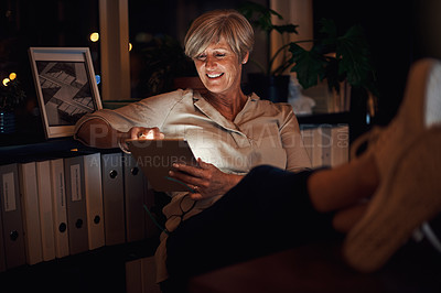 Buy stock photo Cropped shot of an attractive mature businesswoman looking relaxed while using her tablet late at night in the office