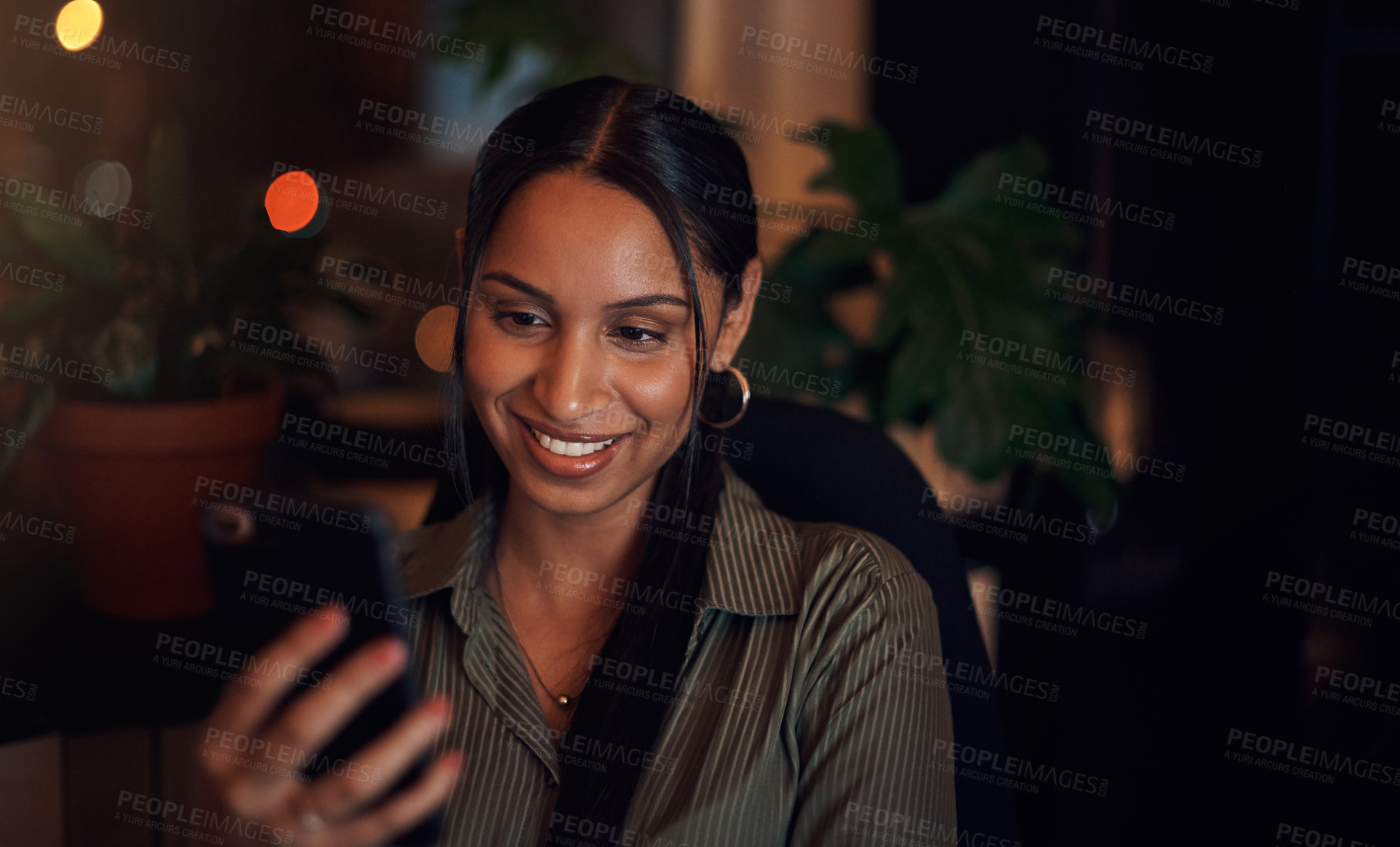 Buy stock photo Shot of a young businesswoman using a cellphone in an office at night