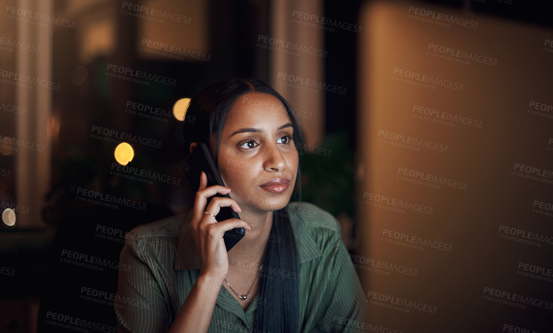 Buy stock photo Shot of a young businesswoman talking on a cellphone while using a computer in an office at night