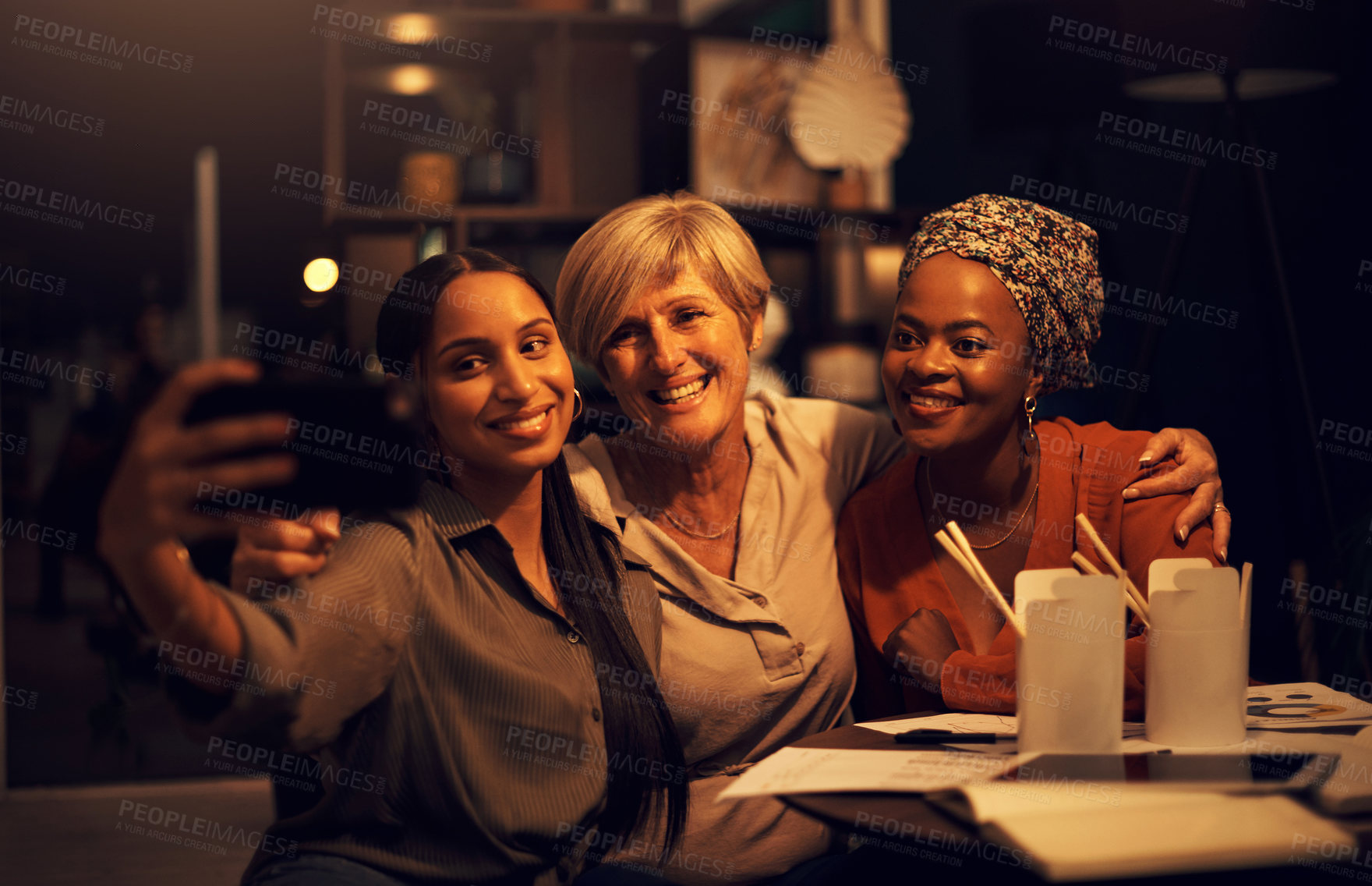 Buy stock photo Shot of a group of businesswomen taking selfies together in an office at night