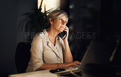 Buy stock photo Shot of a mature businesswoman talking on a cellphone while using a computer in an office at night