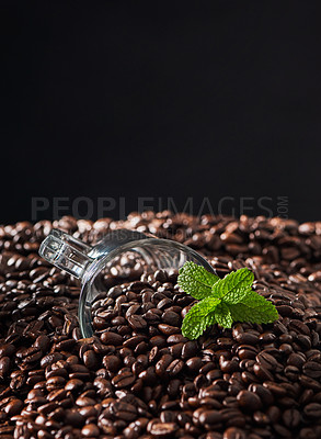 Buy stock photo Closeup shot of a mint leaf and a cup on a pile of coffee beans