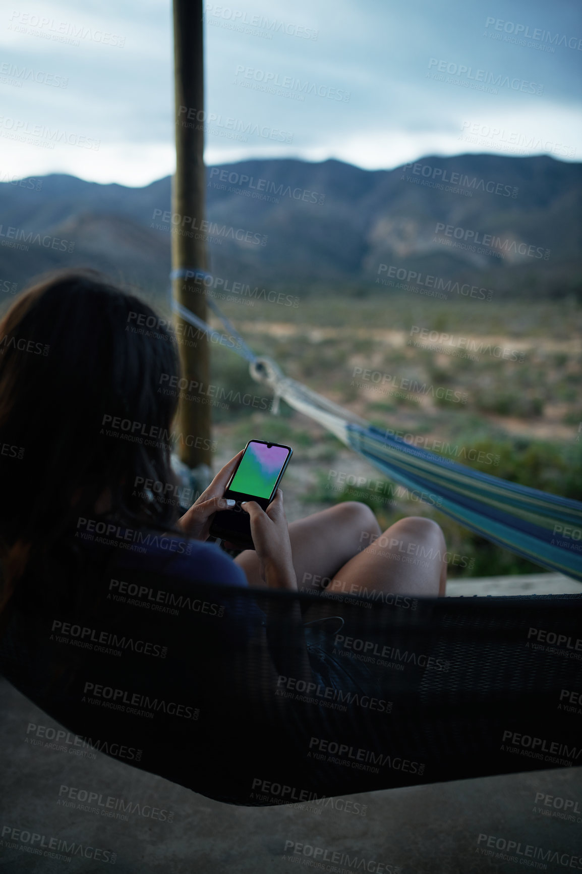 Buy stock photo Shot of an unrecognisable young woman relaxing on a hammock and using a smartphone