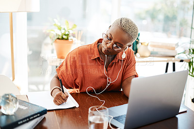 Buy stock photo Shot of a young businesswoman wearing earphones while writing notes in an office
