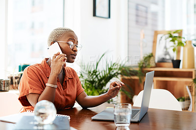 Buy stock photo Shot of a young businesswoman talking on a cellphone while working on a laptop in an office