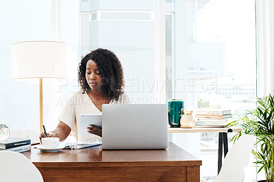 Buy stock photo Shot of a young businesswoman writing notes while working on a digital tablet in an office