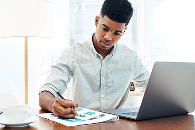 Buy stock photo Shot of a young businessman using a laptop and going over paperwork in a modern office