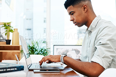 Buy stock photo Shot of a young businessman using a laptop at his desk in a modern office
