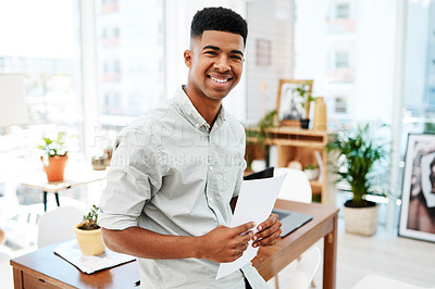 Buy stock photo Portrait of a confident young businessman going over paperwork in a modern office