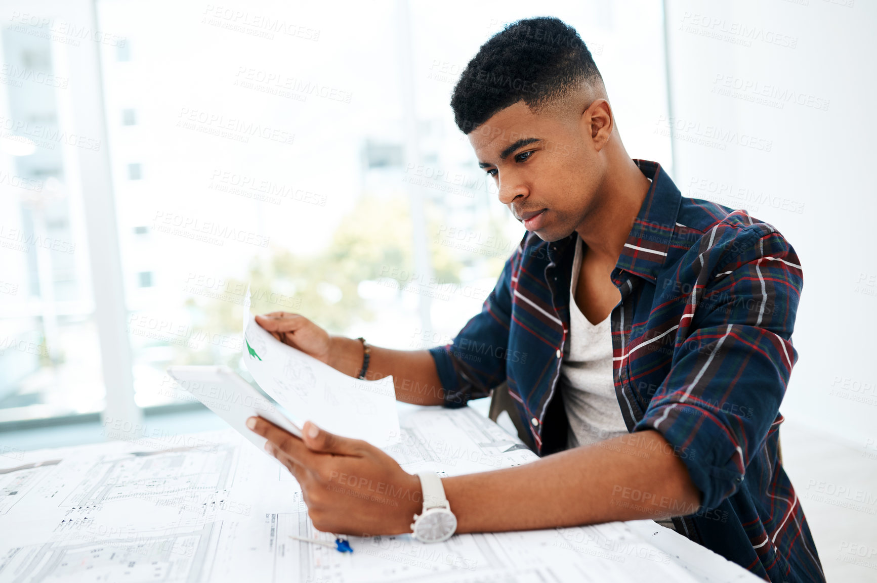 Buy stock photo Shot of a young man going over blueprints in a modern office