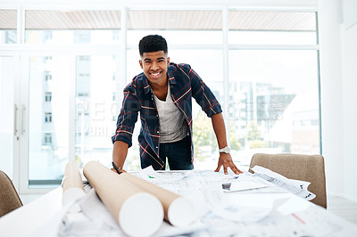 Buy stock photo Portrait of a young man going over blueprints in a modern office