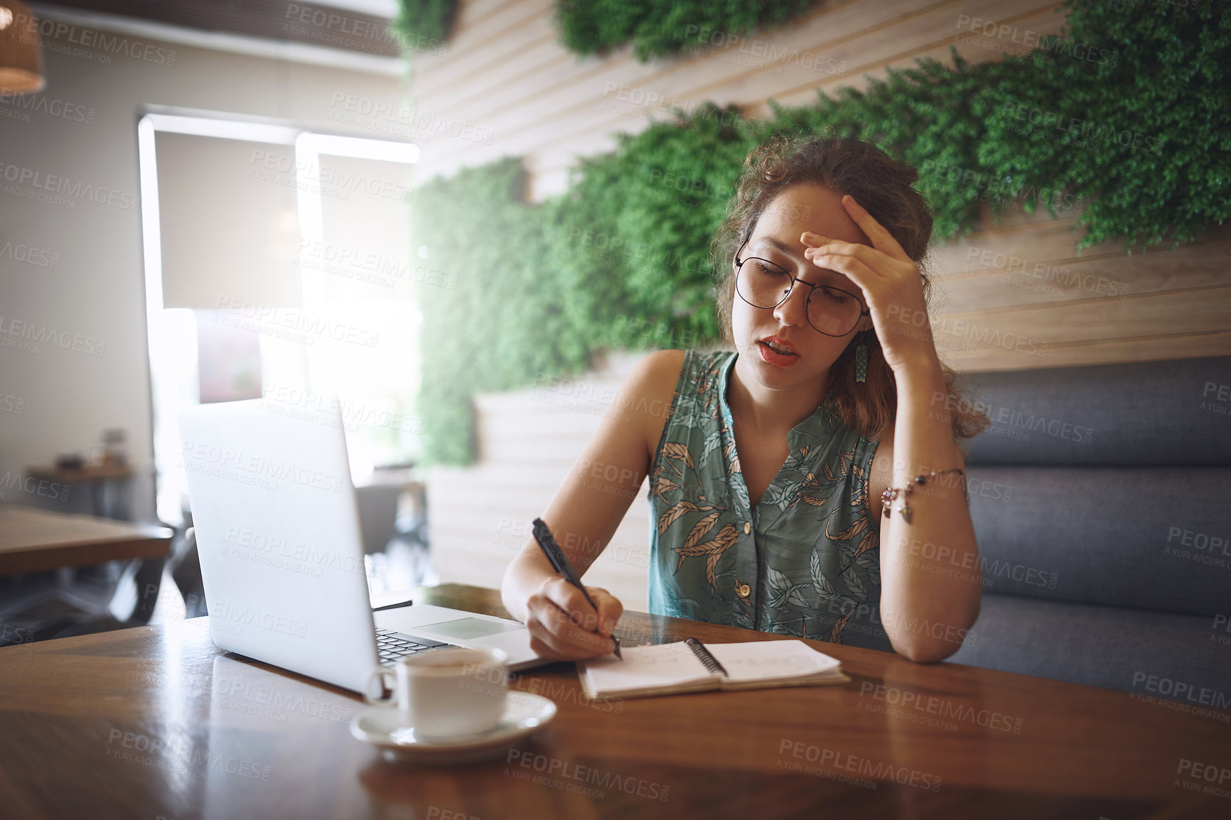 Buy stock photo Shot of a young woman looking stressed while working at a cafe
