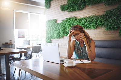 Buy stock photo Shot of a young woman looking stressed using a laptop and smartphone while working at a cafe