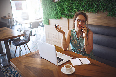 Buy stock photo Shot of a young woman using a laptop and smartphone while working at a cafe