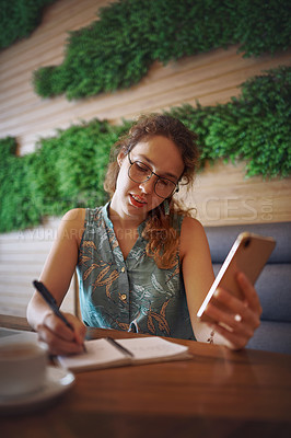Buy stock photo Shot of a young woman using a smartphone while working at a cafe