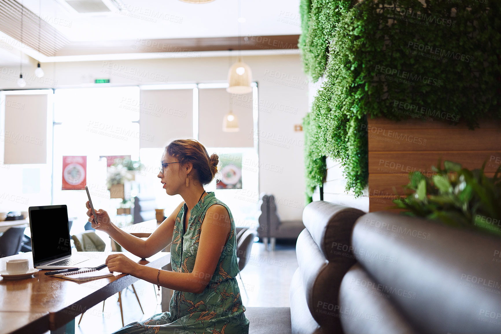 Buy stock photo Shot of a young woman using a laptop and smartphone while working at a cafe